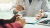 A man in a doctor's coat with a stethoscope around the neck is having a patient sign documentation.
