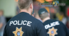 The backs of two police officers are seen. It is known they are part of the police because they are each wearing dark blue t-shirts with the word POLICE in capital white letters and a badge underneath it. This article from Disqualification Appeals explains reasons to be a police officer.